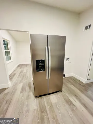 a view of a refrigerator in kitchen and an empty room with wooden floor