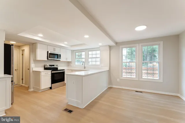 a large white kitchen with stainless steel appliances granite countertop a stove top oven a sink dishwasher a refrigerator and white cabinets with wooden floor
