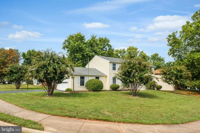 a view of a white house next to a yard with big trees