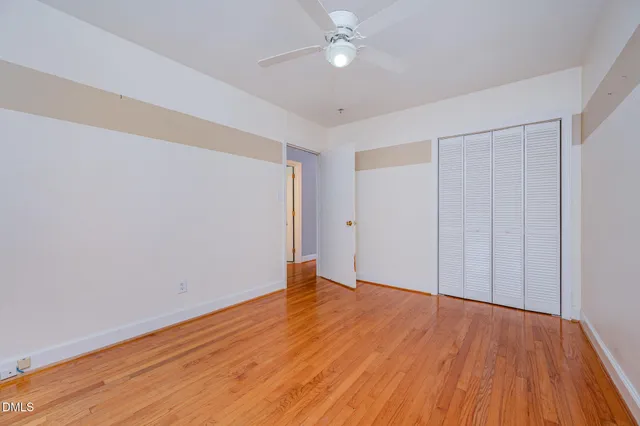 a view of an empty room with wooden floor and fan