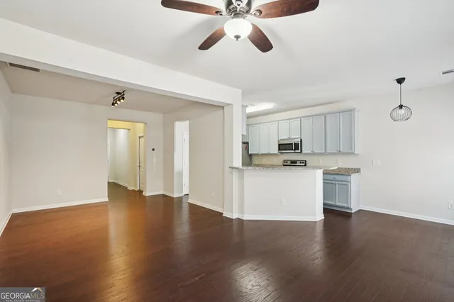 a view of an empty room and kitchen with wooden floor