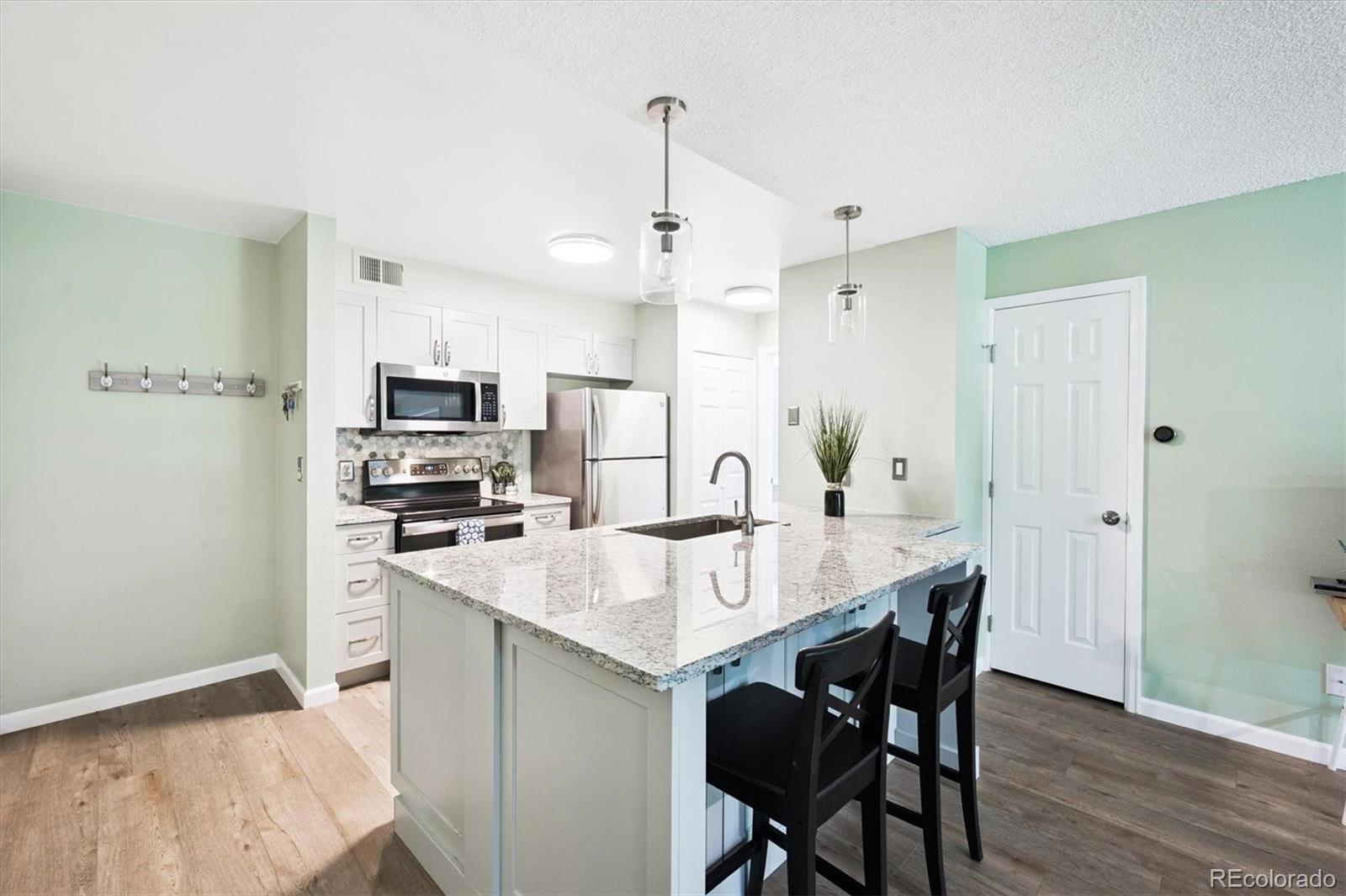 2575 South Syracuse Way, Unit L103 Denver, CO 80231 - Photo 5 of 21 a kitchen with stainless steel appliances a sink a stove a refrigerator with a dining table and chairs