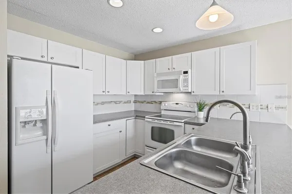 a kitchen with refrigerator a stove a sink and white cabinets with a granite countertops