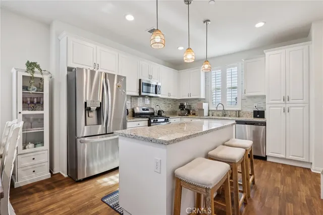 a kitchen with stainless steel appliances granite countertop a refrigerator a sink dishwasher a stove and white cabinets with wooden floor