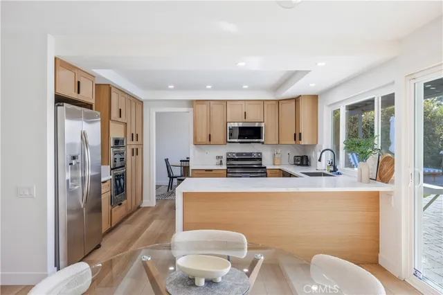 a kitchen with stainless steel appliances a refrigerator a stove a sink dishwasher a dining table and chairs with wooden floor