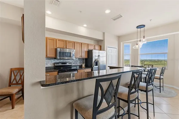 a kitchen with stainless steel appliances kitchen island granite countertop a table chairs and a refrigerator