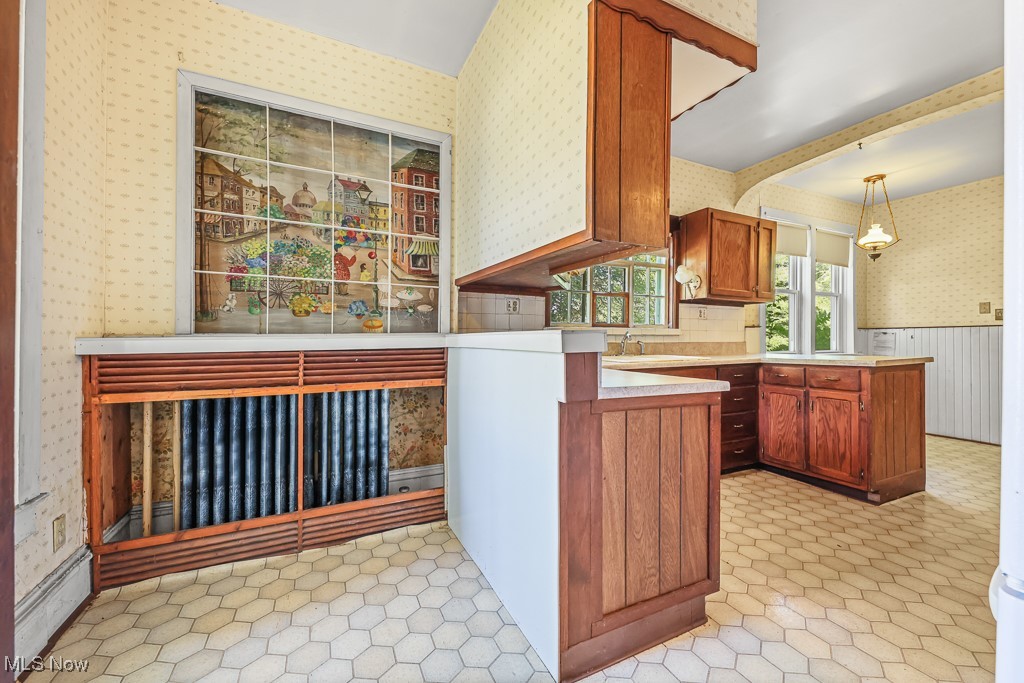 6727 Waterloo Road Atwater, OH 44201 - Photo 19 of 48 Kitchen featuring wallpapered walls, light countertops, brown cabinetry, a peninsula, and wainscoting