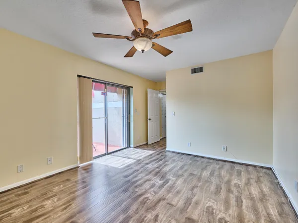 a view of an empty room with wooden floor and a ceiling fan