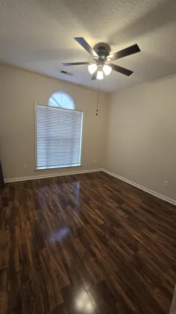 an empty room with wooden floor fan and windows