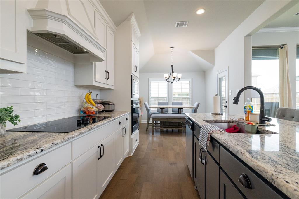 4045 Grove Valley Road Midlothian, TX 76065 - Photo 15 of 34 Two tone kitchen featuring light stone counters, two tone cabinetry, dark wood-style floors, suspended lighting, and stainless steel appliances