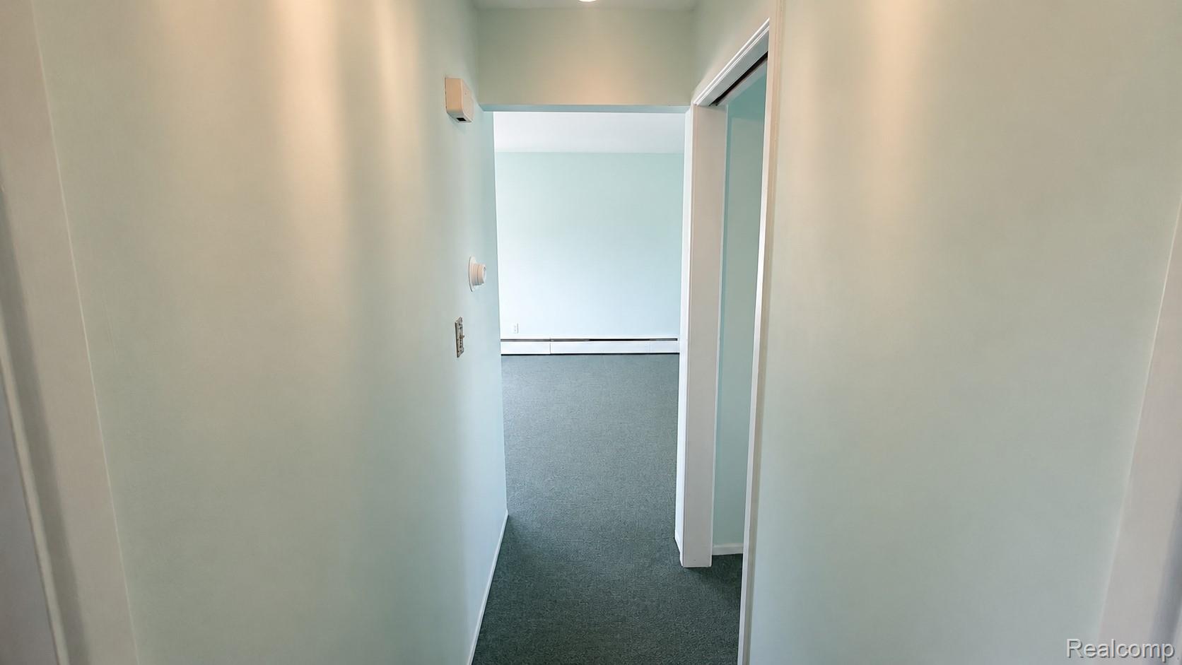 26945 Milford Road, Unit 34 New Hudson, MI 48165 - Photo 12 of 16 Hallway with light green walls and dark green carpeting, featuring a recessed doorway leading to an additional room