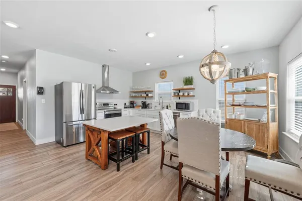 a kitchen with stainless steel appliances granite countertop a stove a refrigerator a kitchen island a dining table and chairs with wooden floor