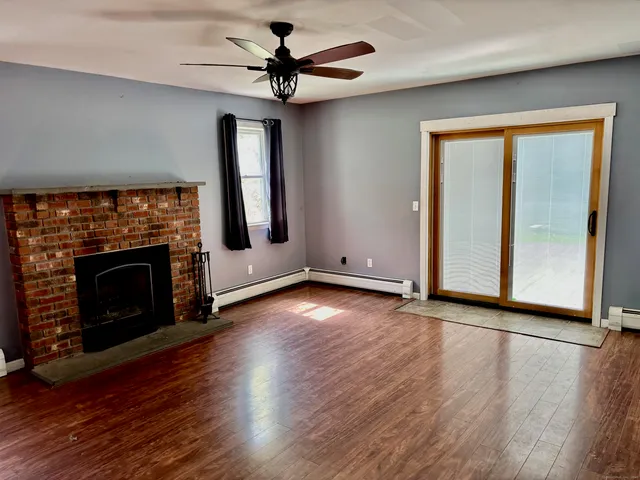 an empty room with wooden floor a fireplace a ceiling fan and a window