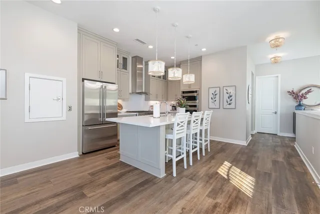 a kitchen with stainless steel appliances kitchen island granite countertop a refrigerator a stove a sink a dining table and chairs with wooden floor
