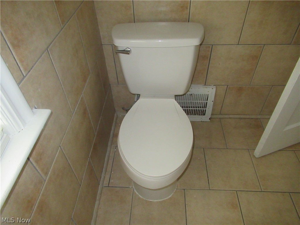 3824 East Antisdale Road Cleveland, OH 44118 - Photo 16 of 27 White toilet with chrome flush lever, set against tan wall and floor tiles