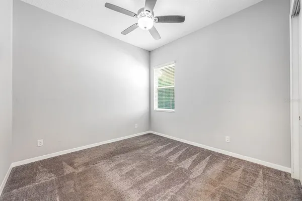 an empty room with a chandelier fan and windows