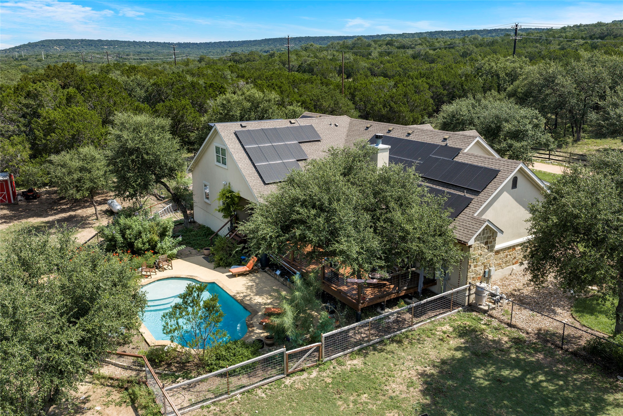 23224 Nameless Road Leander, TX 78641 - Photo 22 of 23 An aerial perspective reveals a charming stucco home with solar panels, a sparkling private pool, and a verdant backdrop of mature trees.