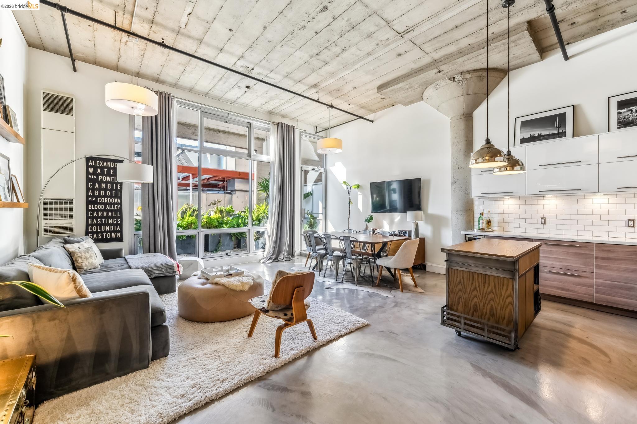 255 3rd Street, Unit 206 Oakland, CA 94607 - Photo 1 of 7 Open concept living area featuring concrete flooring, exposed concrete ceiling, industrial-style column, and full-height windows