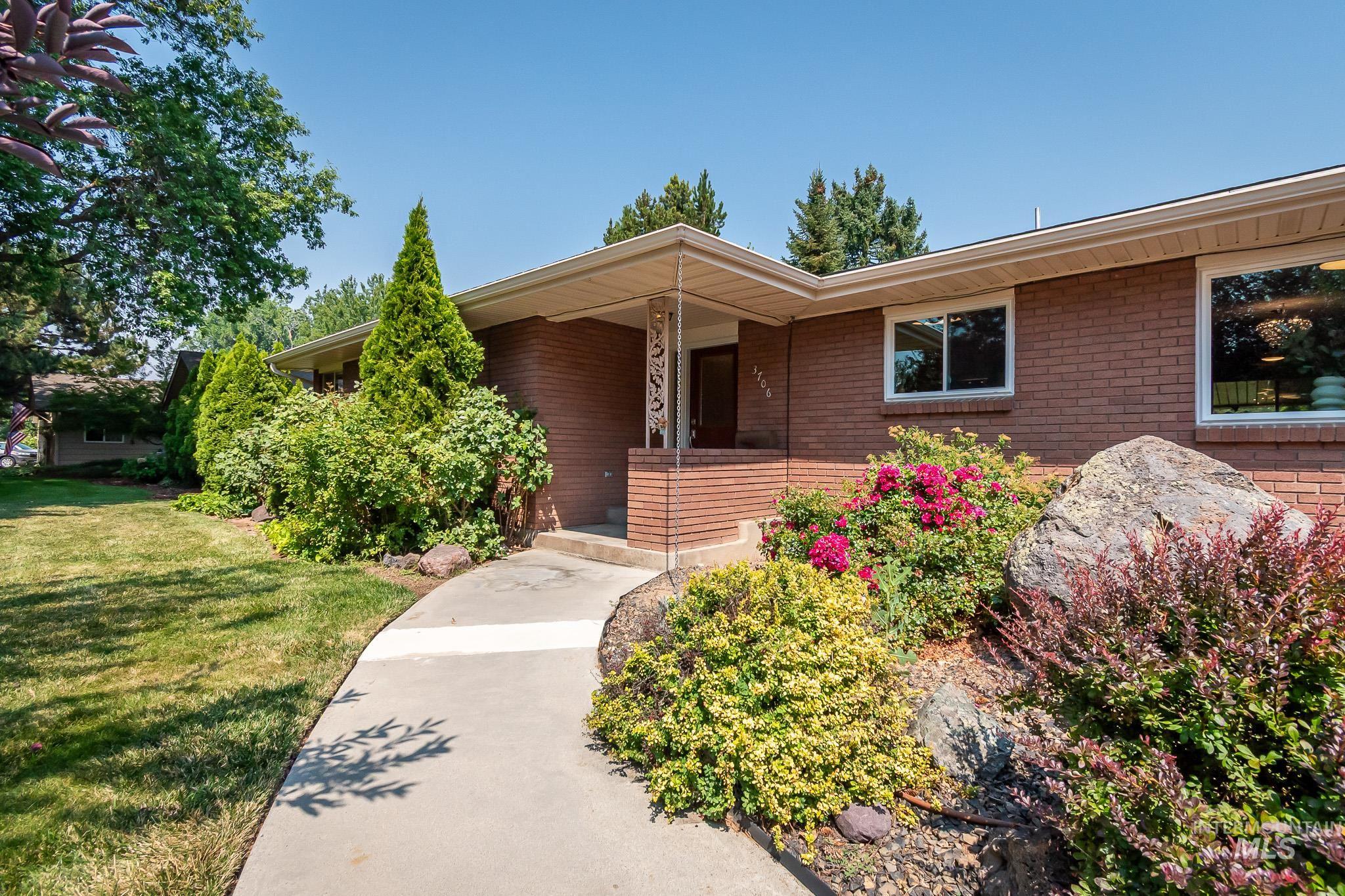 3706 West Clement Road Boise, ID 83704 - Photo 5 of 36 Mid-century brick ranch featuring a welcoming front entry with a covered portico, flanked by vibrant landscape beds with flowering shrubs and ornamental plantings