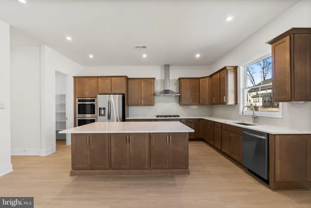 a large kitchen with stainless steel appliances a large counter top a stove a sink and a refrigerator