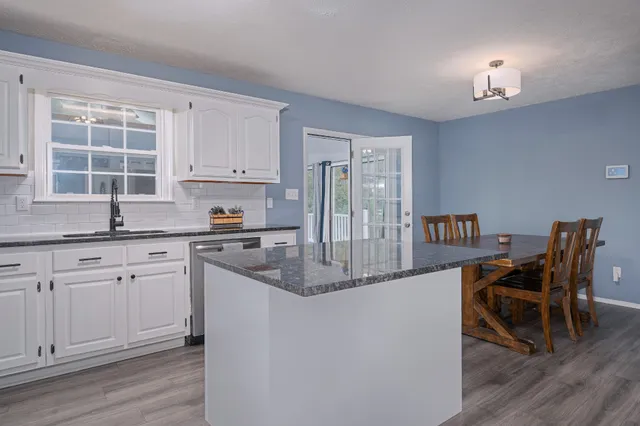 a kitchen with stainless steel appliances granite countertop a stove top oven a sink dishwasher and white cabinets with wooden floor