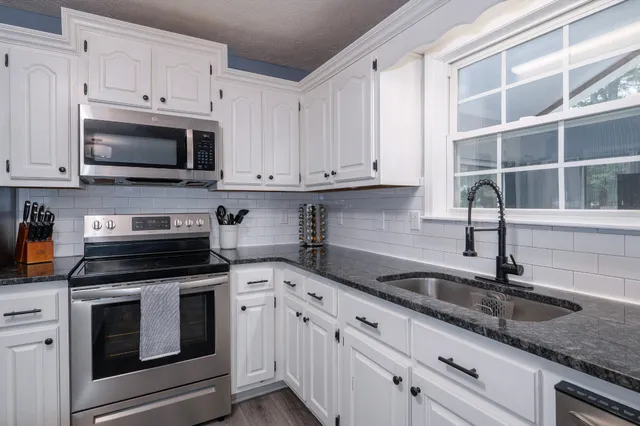 a kitchen with granite countertop white cabinets white stainless steel appliances and a sink