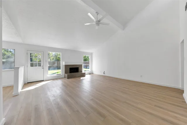 an empty room with wooden floor fireplace and windows