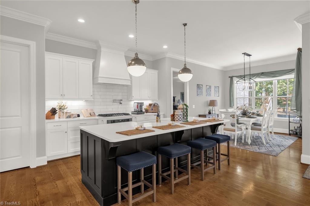 4262 Bridgehead Road Kernersville, NC 27284 - Photo 11 of 50 Kitchen Overview – Light-filled kitchen featuring crisp white cabinetry, subway-tile backsplash, and a contrasting island with seating for four under elegant pendant lighting.