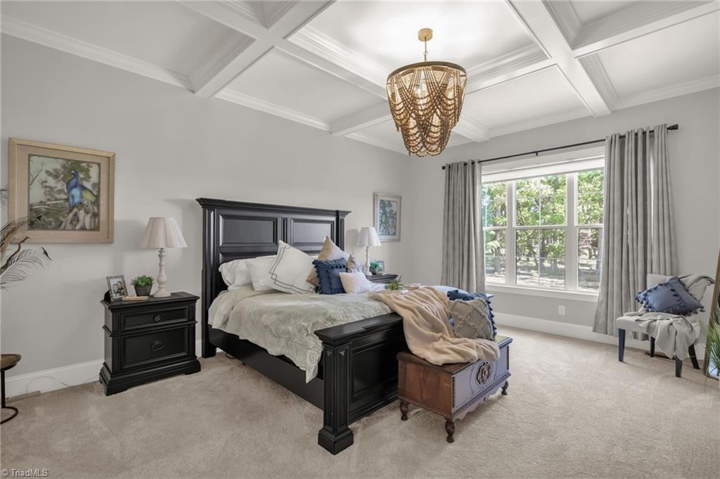4262 Bridgehead Road Kernersville, NC 27284 - Photo 18 of 50 Primary Bedroom – Serene main-level retreat with a coffered ceiling, statement chandelier, and large windows framing peaceful views of the property.