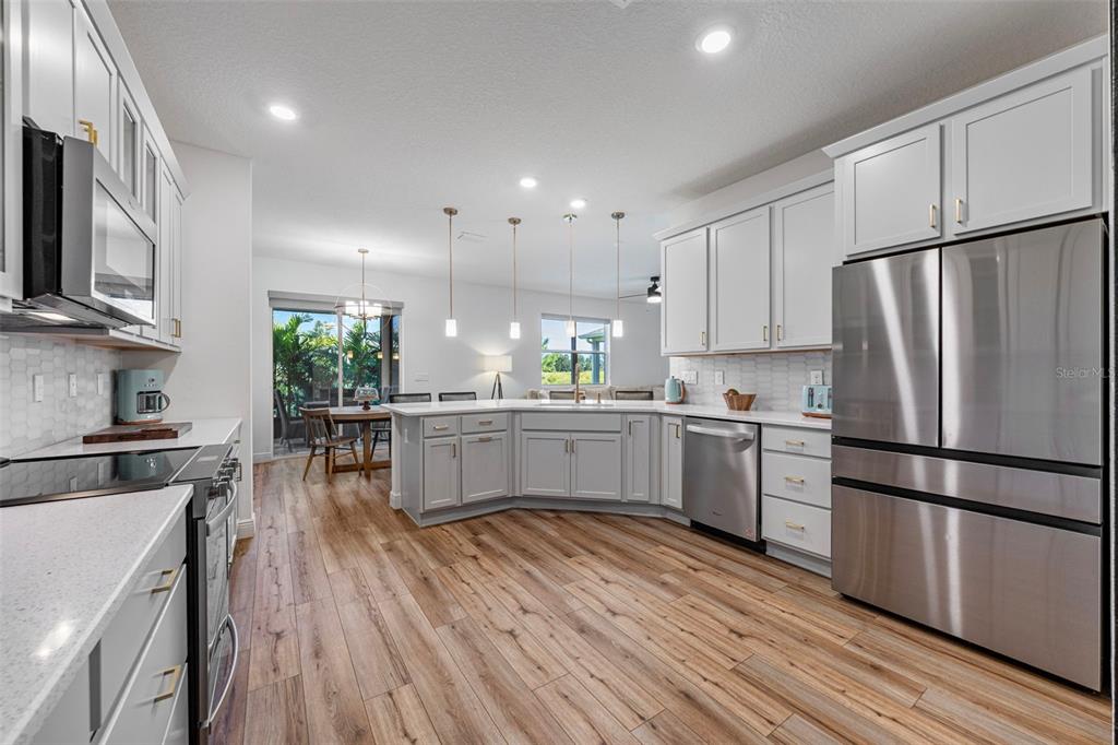11430 Gallatin Trail Parrish, FL 34219 - Photo 5 of 79 a kitchen with a refrigerator a stove top oven a sink dishwasher and white cabinets with wooden floor