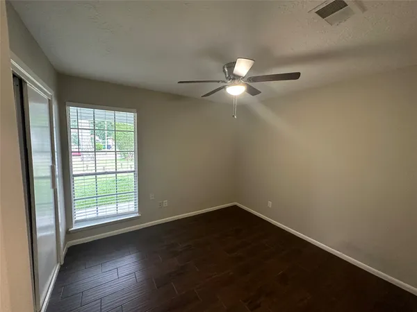 an empty room with wooden floor fan and windows