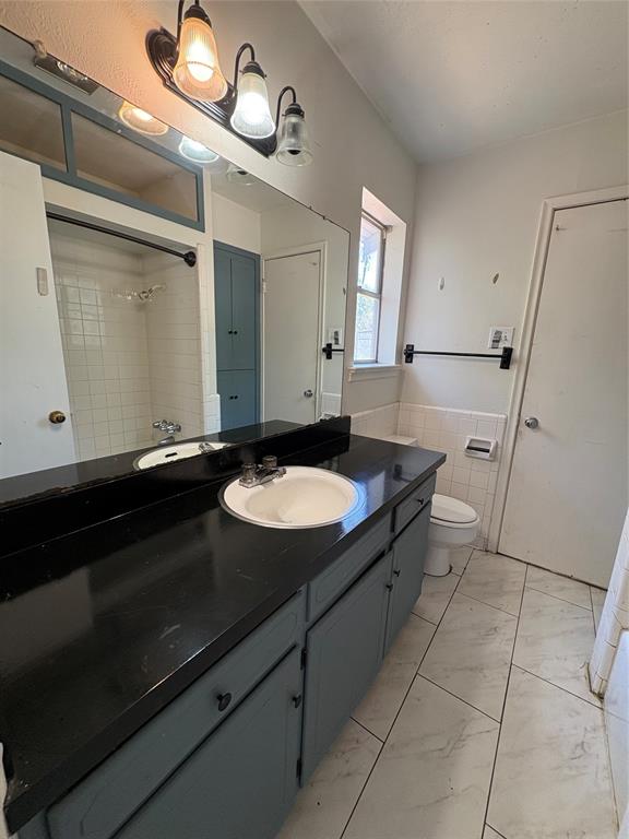 5454 Ranchero Lane Dallas, TX 75236 - Photo 15 of 24 Dual basin vanity with a dark countertop and integrated sinks, white subway tile shower surround, and a built-in storage cabinet