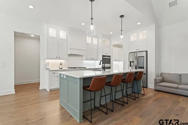 a large kitchen with kitchen island stainless steel appliances a stove a sink a center island and a living room