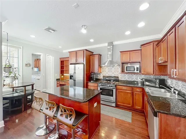 a kitchen with stainless steel appliances granite countertop a stove top oven a sink dishwasher a dining table and chairs with wooden floor