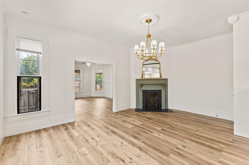 1005 North Trinity Street Decatur, TX 76234 - Photo 12 of 39 Wood-finish flooring throughout, featuring a decorative fireplace with a mantel, a brass chandelier, and white crown molding