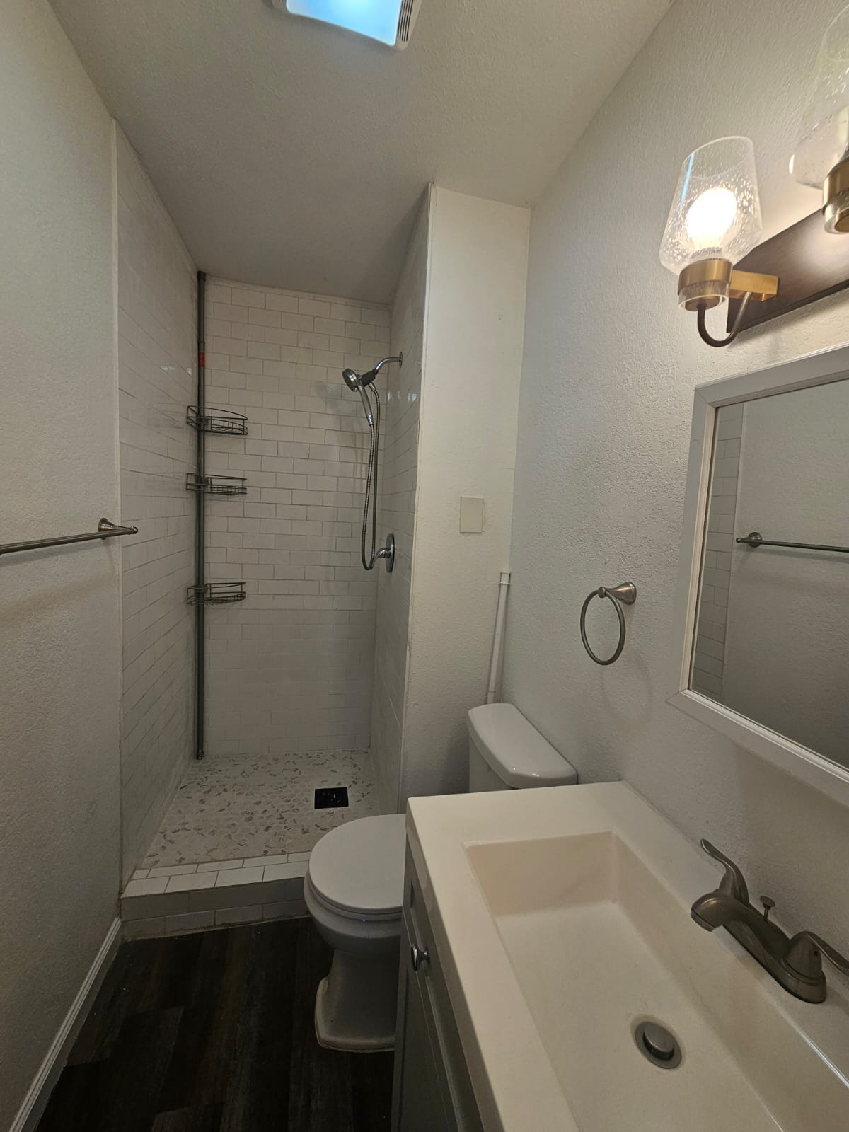 1401 Trinity Street Lockhart, TX 78644 - Photo 18 of 31 Bathroom featuring a walk-in shower with white subway tile surround and pebble-style flooring, a vanity with an integrated sink, and wood-finish flooring