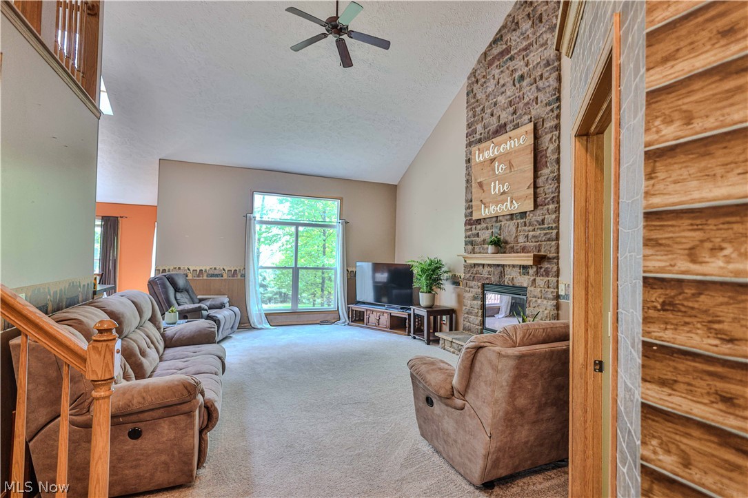 11154 Johnsford Road Southwest Beach City, OH 44608 - Photo 16 of 50 Living area featuring a floor-to-ceiling stone fireplace, vaulted ceiling with a ceiling fan, a large picture window, and light-colored carpeting