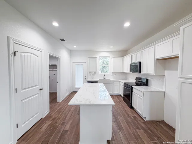 a large kitchen with a center island wooden floor and stainless steel appliances