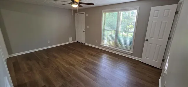 an empty room with wooden floor ceiling fan and windows