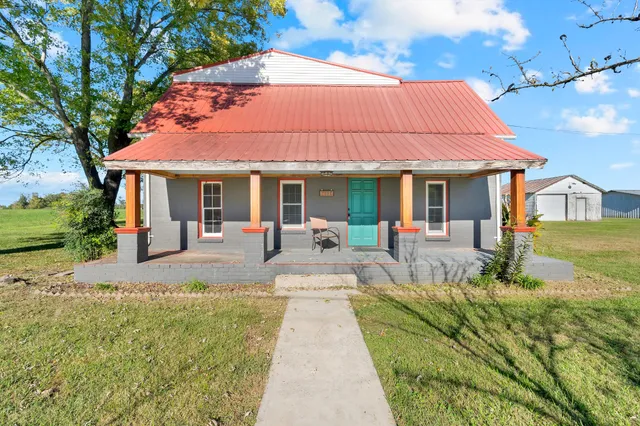 a view of a white house with a big yard plants and large tree