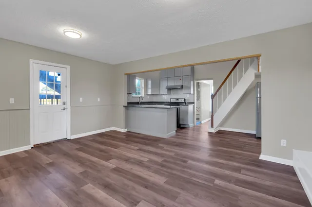 a view of empty room with wooden floor and kitchen