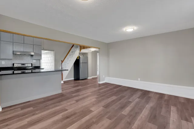 a view of empty room with wooden floor and kitchen