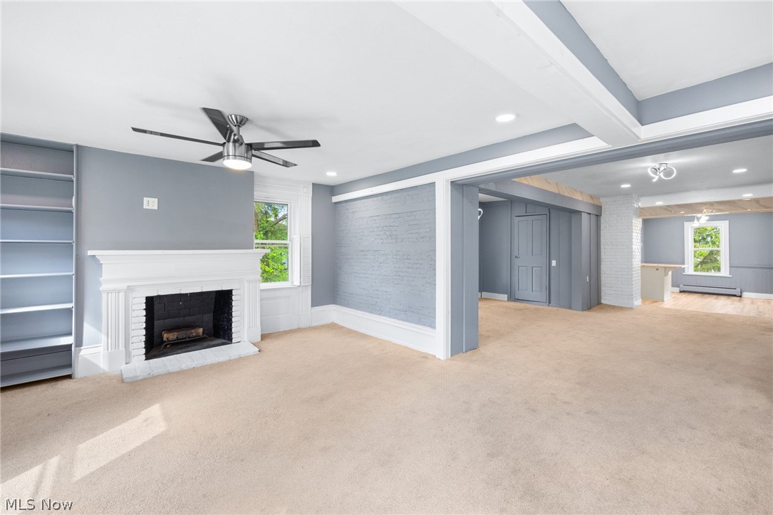 39016 Detroit Road Avon, OH 44011 - Photo 8 of 36 Unfurnished living room featuring light carpet, beamed ceiling, a baseboard heating unit, a brick fireplace, and ceiling fan