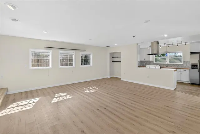 an empty room with wooden floor and kitchen view