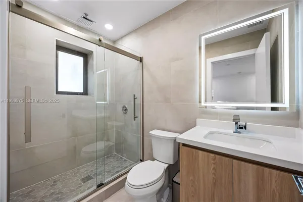 a bathroom with a toilet a sink a glass door a shower and a mirror