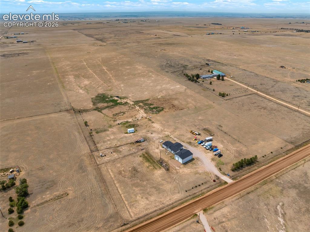 1350 South Calhan Highway Yoder, CO 80864 - Photo 6 of 45 Expansive rural property featuring multiple structures, including a two-story residence with an attached garage, an additional outbuilding, and a second distant structure with a light-colored roof