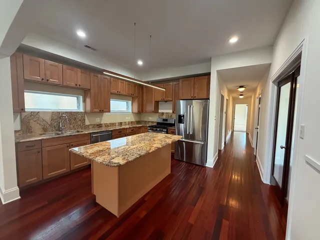 a large kitchen with stainless steel appliances granite countertop wooden floors wooden cabinets a sink and a window
