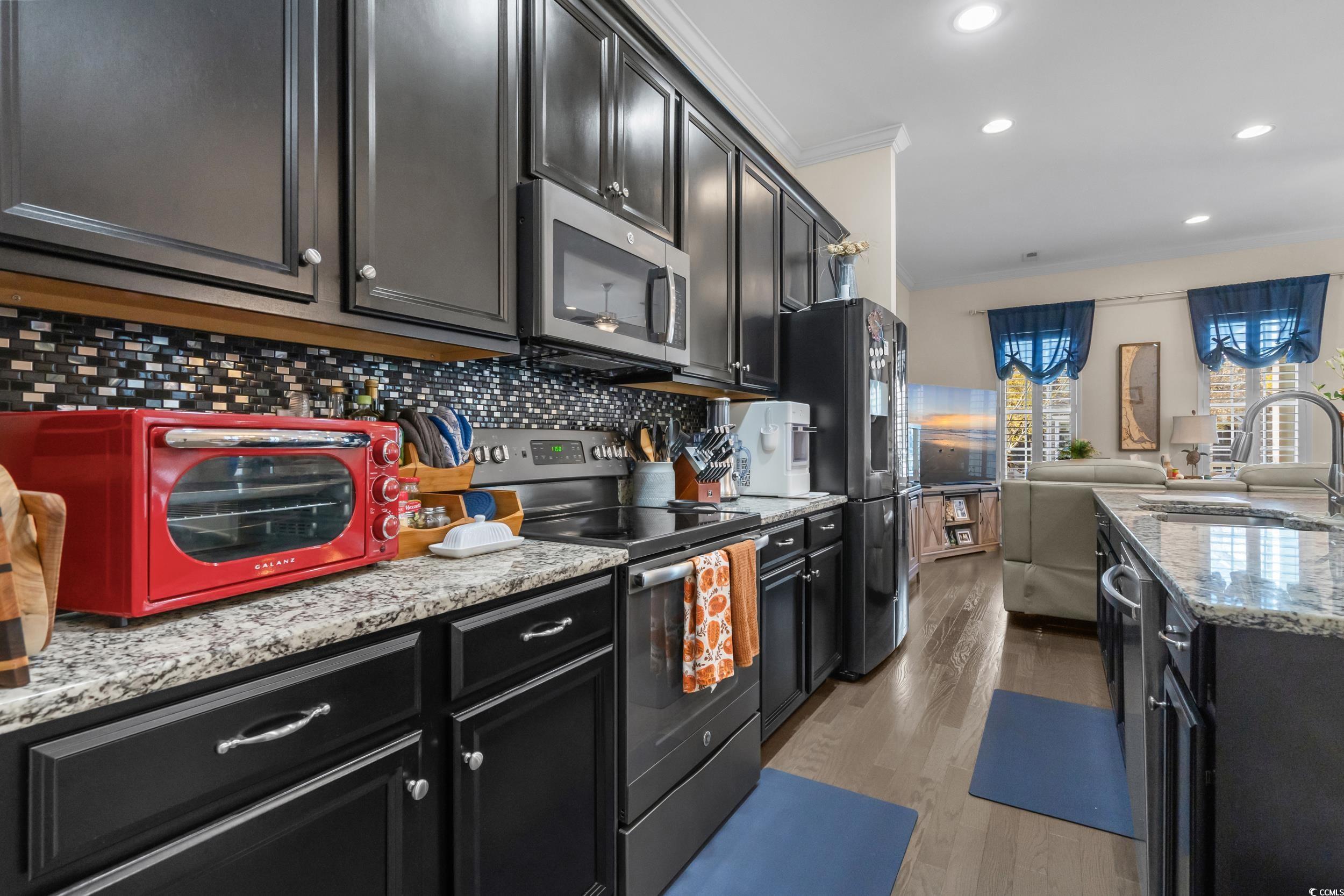2794E Howard Avenue, Unit A Myrtle Beach, SC 29577 - Photo 39 of 40 Kitchen featuring dark cabinets, appliances with stainless steel finishes, light stone counters, open floor plan, and ornamental molding