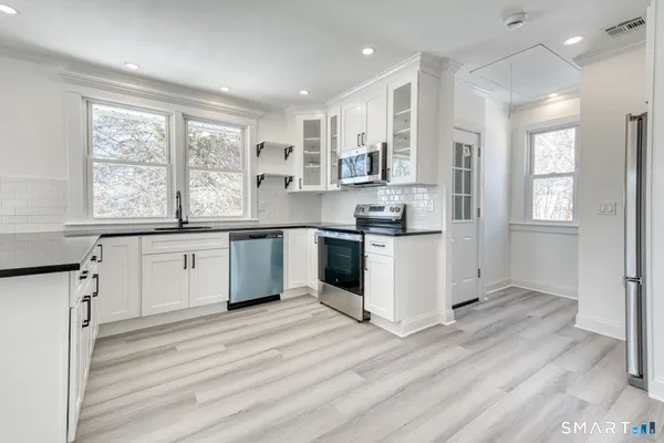 a kitchen with stainless steel appliances granite countertop a stove a sink dishwasher a refrigerator and white cabinets with wooden floor