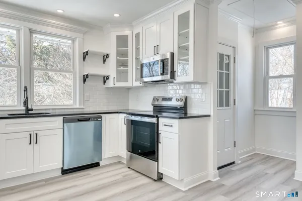a kitchen with stainless steel appliances granite countertop a stove a sink and white cabinets with wooden floor